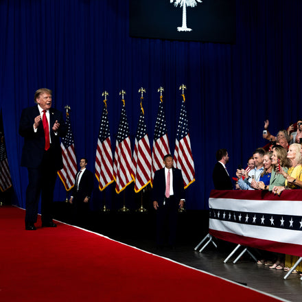 Crowd of supporters at a Donald Trump rally with campaign banners in the background