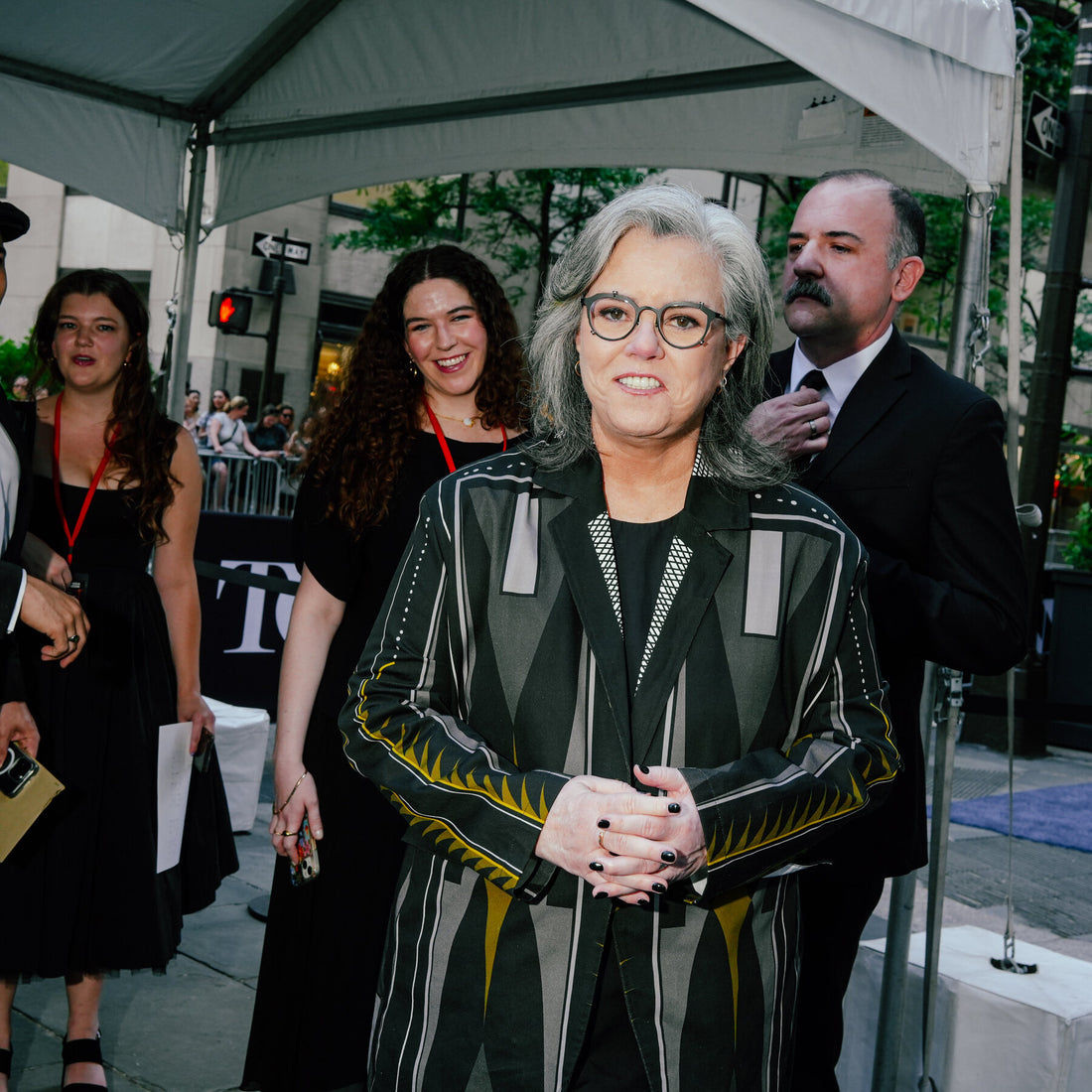 Rosie O'Donnell standing on the Jimmy Kimmel Live! set with a microphone, preparing to deliver a political joke.