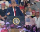 Donald Trump speaking at an Iowa rally with a microphone and American flag backdrop