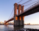 Police officers standing on the Brooklyn Bridge at dawn with a suspect on the cables in view