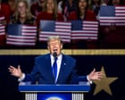 Donald Trump speaking at a rally while holding a sign that reads $5,000 for every American