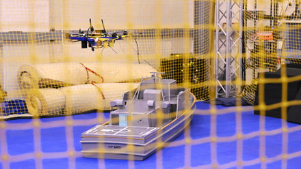 Drone equipped with multiple cameras approaching a naval ship deck in rough seas