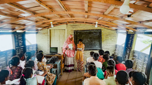 A brightly painted floating school docked on a flooded Bangladeshi river with children boarding the boat.